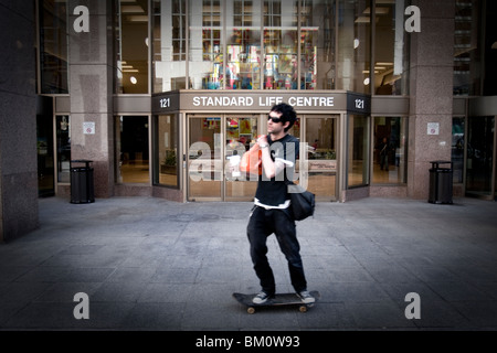 Un uomo su uno skateboard giostre di fronte a standard di vita nel centro di Toronto il quartiere finanziario Foto Stock