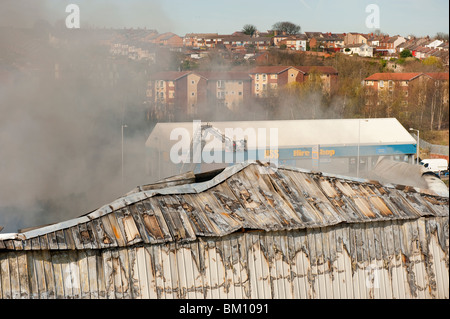 Grande fabbrica e magazzino collassato e a covare dopo un grave incendio notte prima - Vigili del Fuoco basso smorzamento Foto Stock