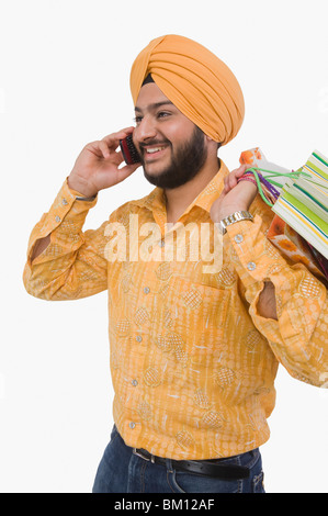 La religione sikh uomo parlando al telefono cellulare e portare una borsa per la spesa Foto Stock