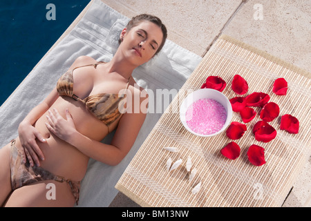 Donna appoggiata con aroma prodotti accanto a lei al bordo della piscina Foto Stock