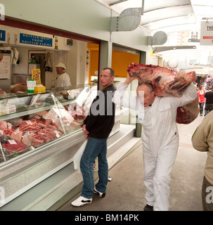 Un macellaio uomo che porta la carne, mercato di Norwich, Norwich, Norfolk, Regno Unito Foto Stock