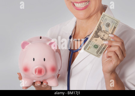 Medico donna in possesso di una nota di valuta e un salvadanaio Foto Stock