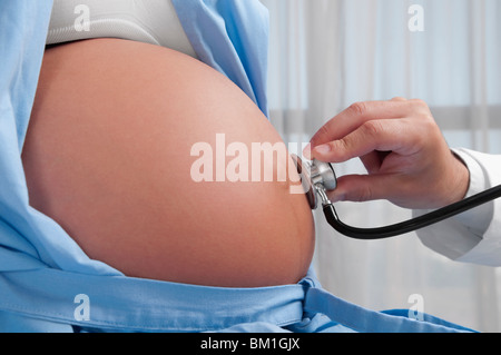 Medico esaminando una donna incinta con uno stetoscopio Foto Stock