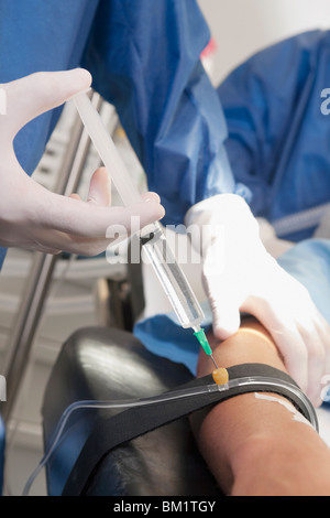 Medico iniettando il braccio del paziente in sala operatoria Foto Stock