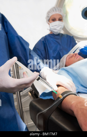 Medico iniettando il braccio del paziente in sala operatoria Foto Stock