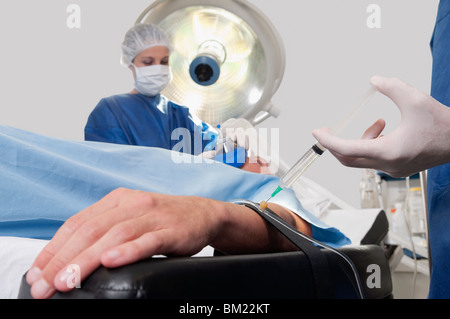 Medico iniettando il braccio del paziente in sala operatoria Foto Stock