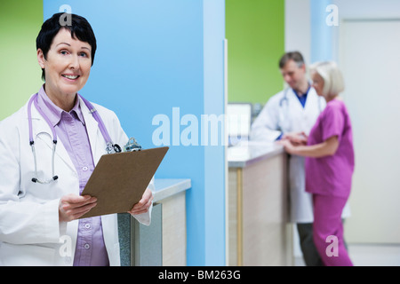 Medico donna tenendo un clipboard con un medico e infermiere in background Foto Stock
