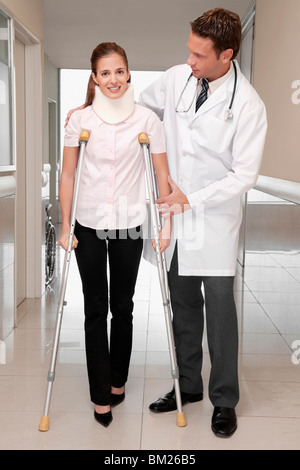 Medico aiutare un paziente a camminare in un corridoio di ospedale Foto Stock