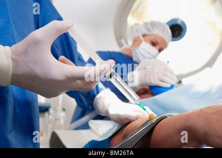 Medico iniettando il braccio del paziente in sala operatoria Foto Stock