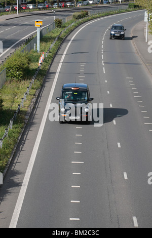 Un nero Londra taxi passa al di sopra di velocizzare i contrassegni e passato un Gatso autovelox sulla A316, grande Chertsey Road, Hounslow, Regno Unito. Foto Stock