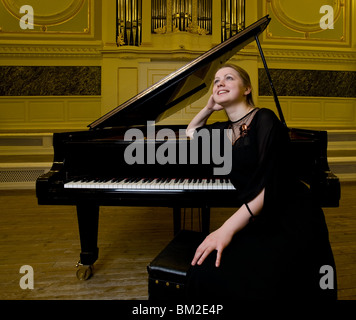 Ragazza vestiti di nero si siede vicino ad un pianoforte e dreamily guarda in alto Foto Stock