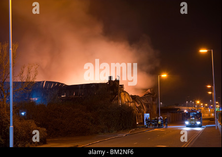 Grande magazzino di fabbrica sul fuoco di notte con un sacco di fiamme e fumo Foto Stock