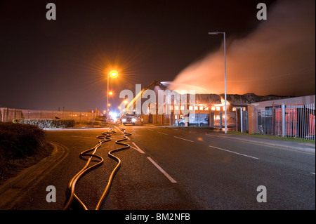Grande magazzino di fabbrica sul fuoco di notte con un sacco di fiamme e fumo Foto Stock
