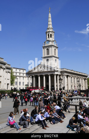 La gente seduta al di fuori della Galleria Nazionale, con la Chiesa di St Martin's nei campi, Trafalgar Square, Londra Inghilterra REGNO UNITO Foto Stock