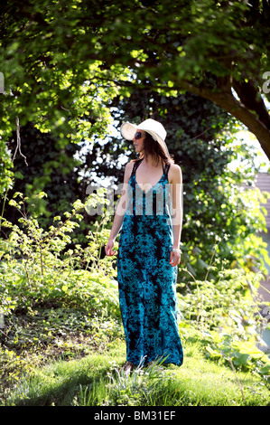 Bella giovane donna in 20s che indossa un abito maxi da pavoni store con un floppy cappello bianco e occhiali da sole REGNO UNITO Foto Stock