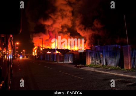 Grande magazzino di fabbrica sul fuoco di notte con un sacco di fiamme e fumo Foto Stock