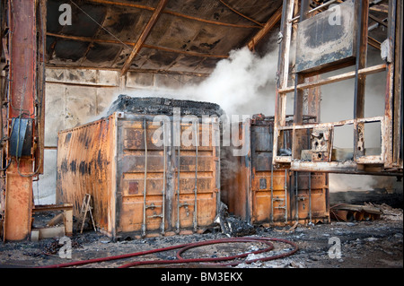 Grande fabbrica e magazzino collassato e a covare dopo un grave incendio notte prima - Vigili del Fuoco basso smorzamento Foto Stock