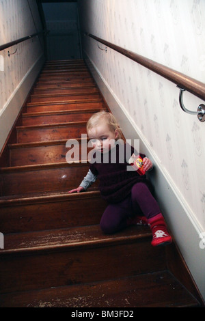 BAMBINO, ARRAMPICATA, SCALE: Una bambina di due anni scende ripide scale pavimenti in legno gradini da soli scatola dolci stivali da calzino modello rilasciato Foto Stock