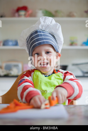 Little Boy divertendosi tritare le carote in un tavolo da cucina. Foto Stock