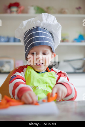 Little Boy divertendosi tritare le carote in un tavolo da cucina. Foto Stock