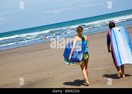 Nuotatori trasportare tavole boogie fino alla spiaggia. Piha, Waitakere gamme Parco Regionale, Auckland, Isola del nord, Nuova Zelanda Foto Stock