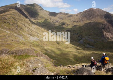 Snowdonia North Wales UK. Persone che camminano giù Yr Aran pendio di montagna con vista panoramica su Cwm Llan a Mount Snowdon e Y Lliwedd Foto Stock