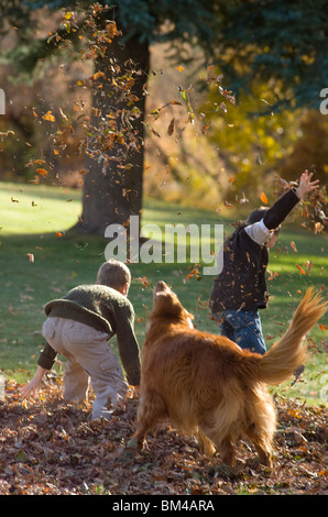 I bambini la rastrellatura e giocando in foglie di autunno con il cane di famiglia Foto Stock