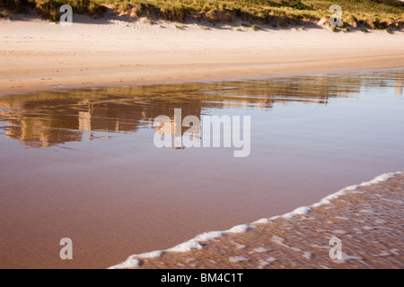 Bamburgh, Northumberland, England, Regno Unito, Europa. Il castello di Bamburgh riflessa nella sabbia bagnata sulla spiaggia vuota foreshore Foto Stock