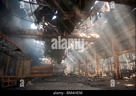 Grande fabbrica e magazzino collassato e a covare dopo un grave incendio notte prima - Vigili del Fuoco basso smorzamento Foto Stock