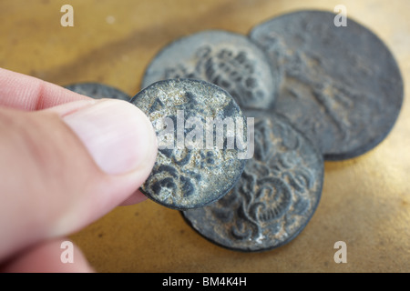 Un uomo azienda antico greco-romana antica monete provenienti dalla Turchia, su una pelle liscia foglio dello sfondo. Foto Stock