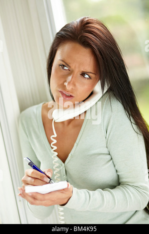 Donna note di scrittura mentre sul telefono Foto Stock