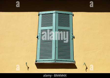 Persiane di legno verde sulla finestra in colore arancio reso sulla parete di edificio di appartamenti in Cannes. Cote d'Azur. Francia Foto Stock