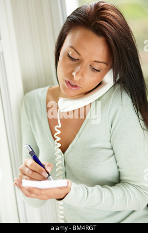 Donna note di scrittura mentre sul telefono Foto Stock