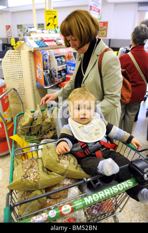 Donna che acquista con il bambino nel carrello del supermercato al momento del check-out Negozio per famiglie del Regno Unito con bambini madre e bambino 2010 Foto Stock