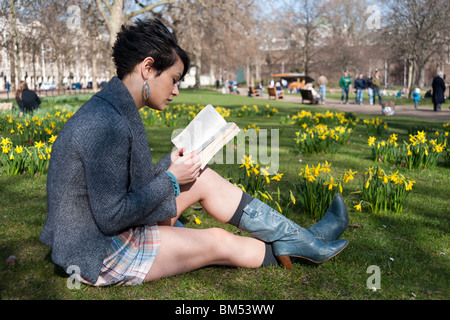 Giovane donna leggendo un libro in St James Park, Londra, Inghilterra, Regno Unito Foto Stock