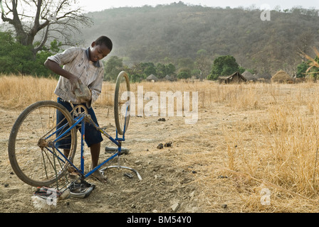 Bassari boy che fissa la sua bicicletta con una roccia, villaggio di Ibel, paese Bassari, Senegal Africa. Foto Stock