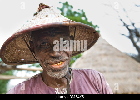 Vecchio Bassari uomo con cappello spiritoso guardando la telecamera, villaggio di Ibel, paese Bassari, Senegal Africa. Foto Stock