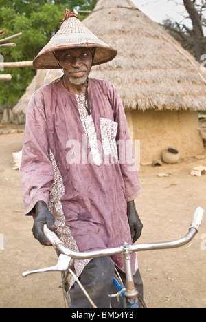 Vecchio Bassari uomo con cappello spiritoso e cerchi di bicicletta per la fotocamera, villaggio di Ibel, paese Bassari, Senegal Africa. Foto Stock