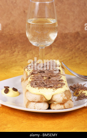 Tiramisù servito su una piastra bianca e decorate con il cioccolato grattugiato. Bicchiere di spumante bianco vino in background. Foto Stock
