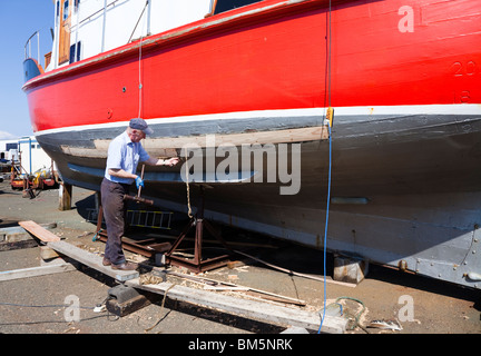 Nave Master builder, John Gaff, riparazione dello scafo di una barca da pesca con il tradizionale metodo di imballaggio oakum negli interstizi Foto Stock