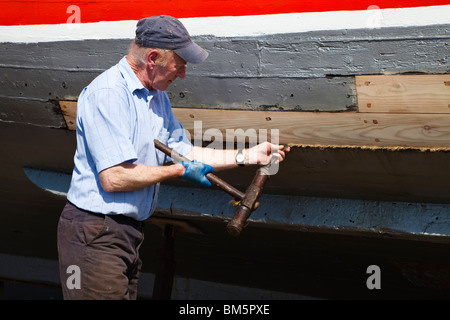 Nave Master builder, John Gaff, riparazione dello scafo di una barca da pesca con il tradizionale metodo di imballaggio oakum negli interstizi Foto Stock