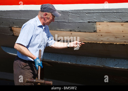 Maestro artigiano costruttore navale la riparazione di legno con scafo di una imbarcazione, servendosi di un martello di cianfrinatura e ferro di cianfrinatura e oakum alla guarnizione di tenuta Foto Stock