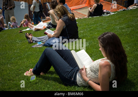 Una donna che legge il suo libro di stampa come una donna usa il suo Amazon Kindle libro elettronico dietro di lei in New York Foto Stock