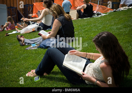 Una donna che legge il suo libro di stampa come una donna usa il suo Amazon Kindle libro elettronico dietro di lei in New York Foto Stock