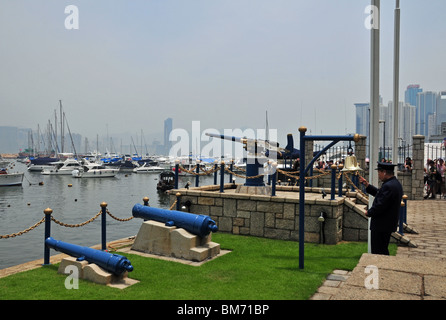 Uomo in marina cerimoniale uniforme blu e cappuccio suonando il campanello prima di sparare il Mezzogiorno pistola, la Causeway Bay di Hong Kong Foto Stock