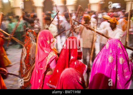 Donna celebra la festa di holi colpendo i maschi con bastoni Foto Stock