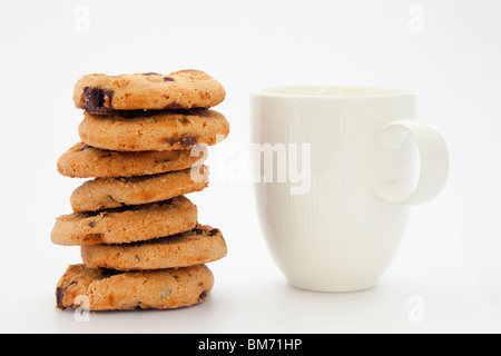 Pila pila di chip di cioccolato biscotti e white tazza di tè o caffè su uno sfondo semplice. Inghilterra, Regno Unito, Gran Bretagna Foto Stock