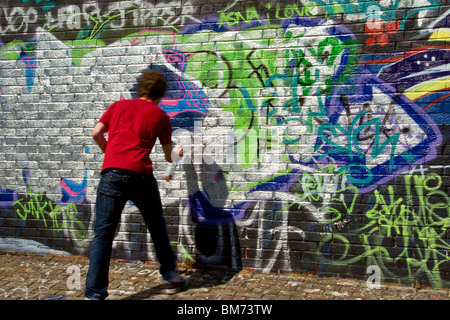 Giovane artista verniciatura a spruzzo su un legalizzato il muro di graffiti a Dundee, Regno Unito Foto Stock