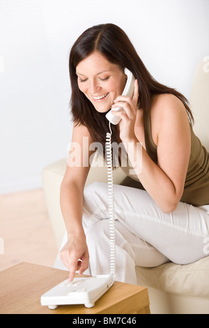 Sul telefono home: donna sorridente di comporre il numero di chiamata nel salotto lounge Foto Stock