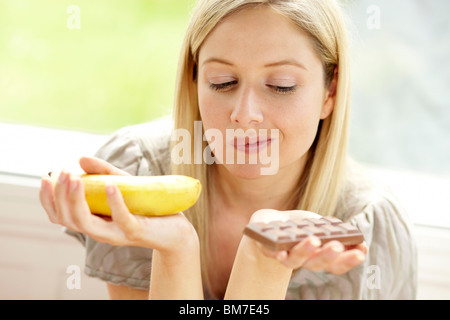 Donna di decidere tra frutta e cioccolata Foto Stock